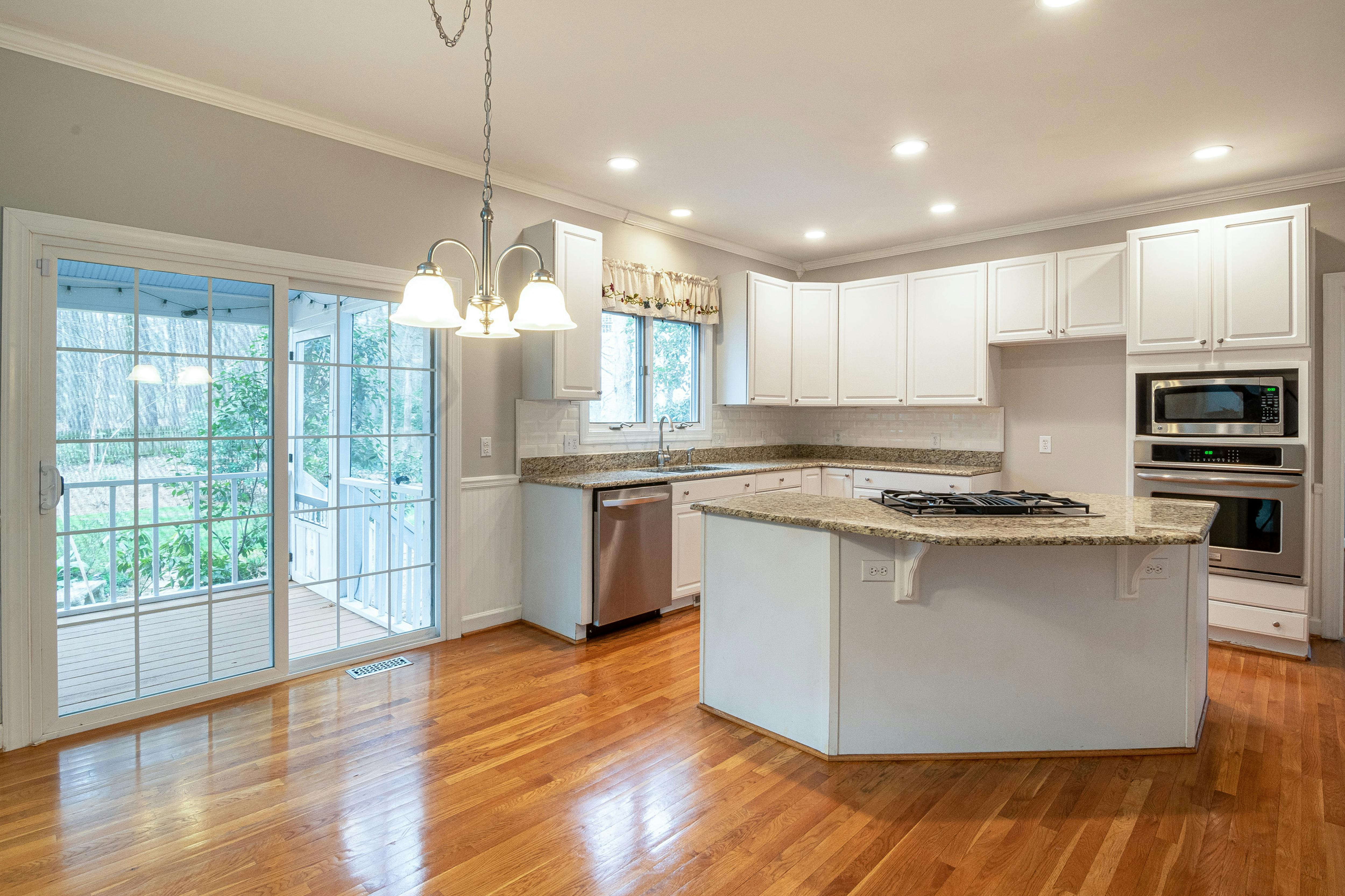 Cocina luminosa con acabados en granito, muebles blancos y piso de madera cálida